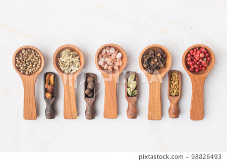 Various spices and green herbs in wooden spoons on white table 98826493
