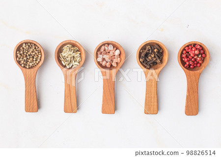 Various spices and green herbs in wooden spoons on white table 98826514