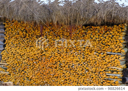 A large amount of split firewood piled up in a large neat stack along the wall of a thatched house A large amount of split firewood piled up in a large neat stack along the wall of a thatched house 98826614