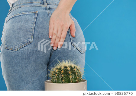 Woman sitting down on cactus against light blue background, space for text. Hemorrhoid concept Woman sitting down on cactus against light blue background, space for text. Hemorrhoid concept 98826770