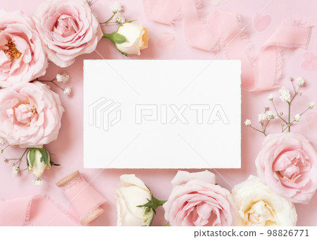 Blank paper card between pink roses and pink silk ribbons on pink top view, wedding mockup Blank paper card between pink roses and pink silk ribbons on pink top view, wedding mockup 98826771