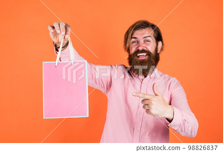 Outgoing man choosing product. happy bearded man with present pack. brutal hipster hold gift. paper shopping bag. birthday surprise at party. man with package. prepare for holidays. best sale offer 98826837