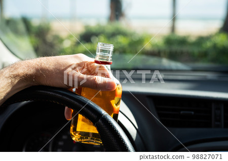 Driver driving a car with a bottle of alcohol in his hands close-up. Driver driving a car with a bottle of alcohol in his hands close-up. 98827071