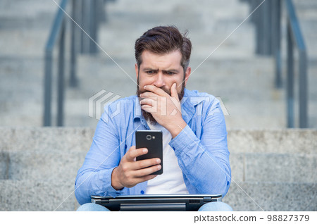 Disappointed man lost bet. Upset man checking up betting results in mobile phone. Betting online Disappointed man lost bet. Upset man checking up betting results in mobile phone. Betting online 98827379