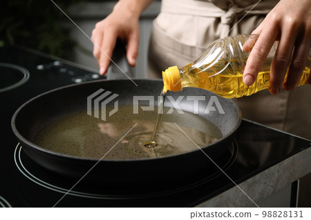 Woman pouring cooking oil from bottle into frying pan, closeup 98828131
