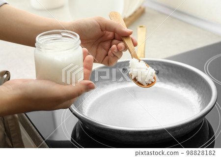 Woman cooking with coconut oil on induction stove, closeup Woman cooking with coconut oil on induction stove, closeup 98828182