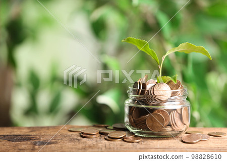 Money and sprout on wooden table against green blurred background, space for text 98828610
