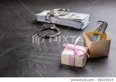 Dollar bills, gift box and handcuffs on grey stone table, space for text. Bribe concept 98828614