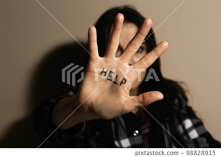 Abused young woman showing palm with word HELP near beige wall, focus on hand. Domestic violence  98828915