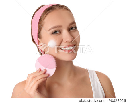 Young woman washing face with brush and cleansing foam on white background. Cosmetic products Young woman washing face with brush and cleansing foam on white background. Cosmetic products 98828926