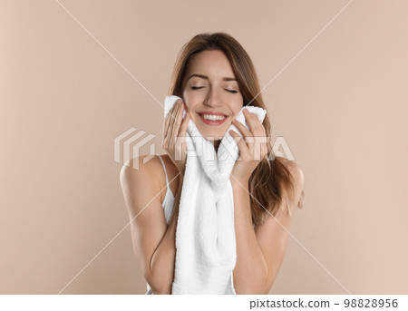 Young woman wiping face with towel on beige background Young woman wiping face with towel on beige background 98828956