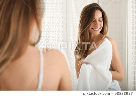 Young woman wiping body with towel near mirror indoors Young woman wiping body with towel near mirror indoors 98828957