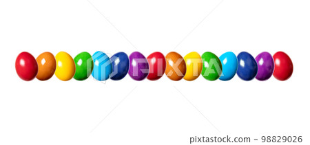Row of slightly twisted, colorful dyed eggs. Line of hard boiled and multi colored chicken eggs. Traditionally used during Easter time as gift or for decoration. Front view, close-up, isolated, photo. Row of slightly twisted, colorful dyed eggs. Line of hard boiled and multi colored chicken eggs. Traditionally used during Easter time as gift or for decoration. Front view, close-up, isolated, photo. 98829026