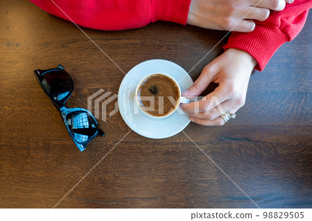 Woman hand holding a Turkish coffee on wooden table. Woman hand holding a Turkish coffee on wooden table. 98829505
