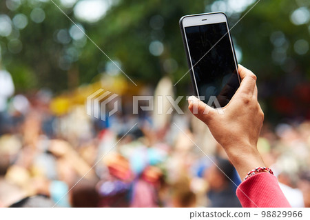Close-up of a hand from the crowd filming the event on a cell phone 98829966