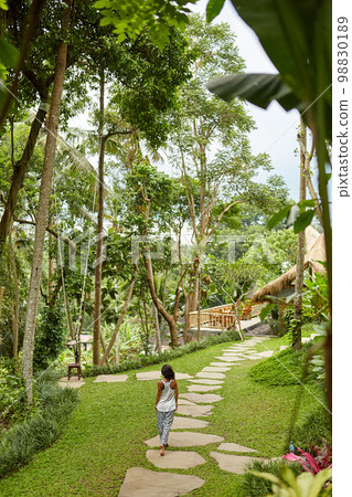 A slender girl walks along a stone path in a tropical garden on the island of Bali 98830189
