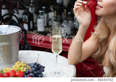 Young Woman sitting with Champagne near table with bottle in bucket and fruits 98830792