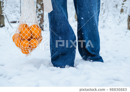 a man holds a wicker bag with tangerines next to his feet in the snow a man holds a wicker bag with tangerines next to his feet in the snow 98830883