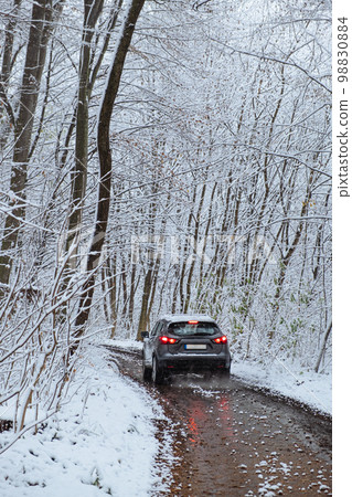 A car with its roof made of snow drives along the road in the middle of a winter forest A car with its roof made of snow drives along the road in the middle of a winter forest 98830884