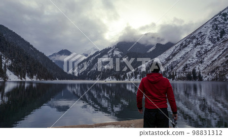 The guy standing on the pier admires mountain lake 98831312