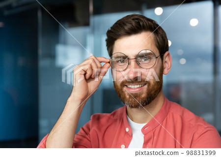 Close-up portrait of young businessman in red shirt, mature man in glasses smiling and looking at camera inside office near window, successful investor happy with achievements and good investment. Close-up portrait of young businessman in red shirt, mature man in glasses smiling and looking at camera inside office near window, successful investor happy with achievements and good investment. 98831399