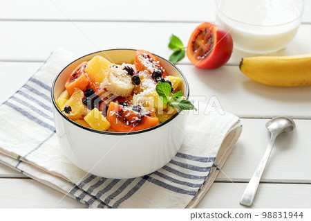 Bowl of fresh fruit salad with coconut flakes and yoghurt in the background Bowl of fresh fruit salad with coconut flakes and yoghurt in the background 98831944