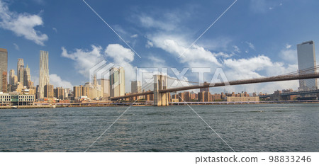 Panorama of the Brooklyn Bridge with a beautiful cloudy sky against the backdrop of the skyscrapers of Manhattan overlooking the East River 98833246