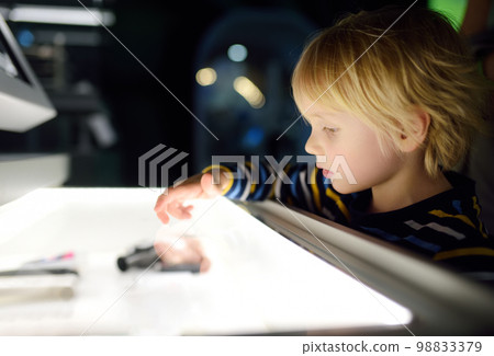 Little caucasian boy is looking an exposition in a scientific museum. Keen child is exploring of exhibits. Education and entertainment for children. Activities for family with kids. 98833379