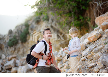 Cute schoolchild and his mature father hiking together on mountain and exploring nature. Dad and son spend quality time together.Concepts of adventure and hiking tourism 98833406