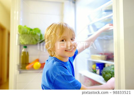 Cute preteen boy independently taking products from refrigerator at home. Child choosing between healthy and unhealthy food. Intuitive nutrition, conscious nutrition Cute preteen boy independently taking products from refrigerator at home. Child choosing between healthy and unhealthy food. Intuitive nutrition, conscious nutrition 98833521
