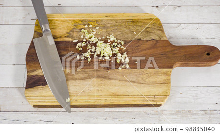 Mincing organic garlic on a wood cutting board. Mincing organic garlic on a wood cutting board. 98835040