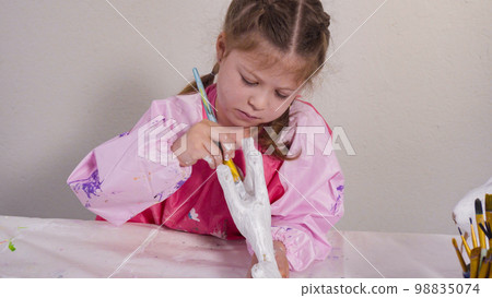 Little girl painting paper mache figurine at homeschooling art class. Little girl painting paper mache figurine at homeschooling art class. 98835074