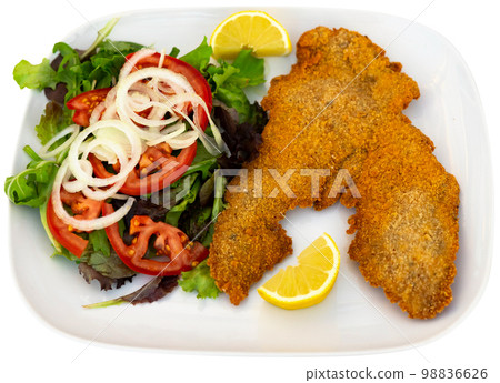 Portion of breaded cutlet, milanesa, with salad served on table 98836626