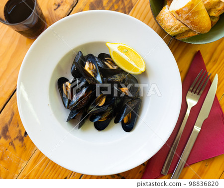 Baked mussels in shells on plate with slice of lemon 98836820