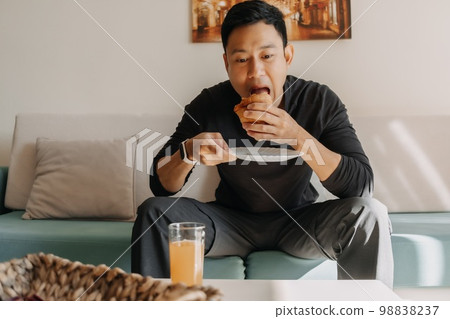 Man having bread and juice as breakfast on the sofa living room. Man having bread and juice as breakfast on the sofa living room. 98838237