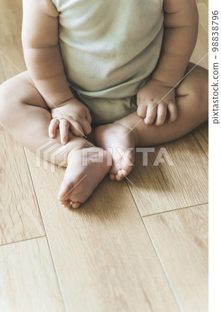 Baby sits on a wooden laminate floor. Bare legs and feet of a baby in the living room floor Baby sits on a wooden laminate floor. Bare legs and feet of a baby in the living room floor 98838796