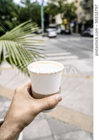 Takeaway coffee in a paper cup. A hand with a drink to go on the background of street. Paper cup mockup Takeaway coffee in a paper cup. A hand with a drink to go on the background of street. Paper cup mockup 98838797