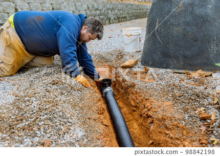 Assembling drainage pipe for rain water that is going to be used for rain water collection on covered parking space with gravel driveway Assembling drainage pipe for rain water that is going to be used for rain water collection on covered parking space with gravel driveway 98842198