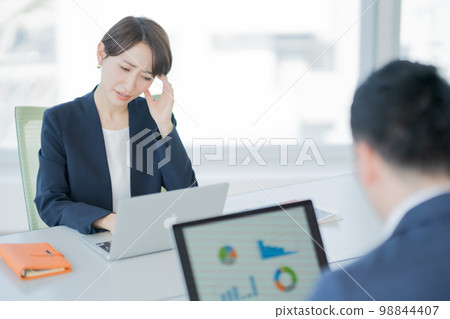 一個年輕的女人在公司裡抱著她的頭 98844407