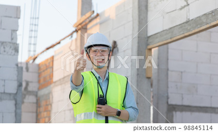 Professional engineer inspecting the construction of a house or factory building and giving a thumbs up showing readiness and good performance, Engineer's safety suit and helmet. 98845114