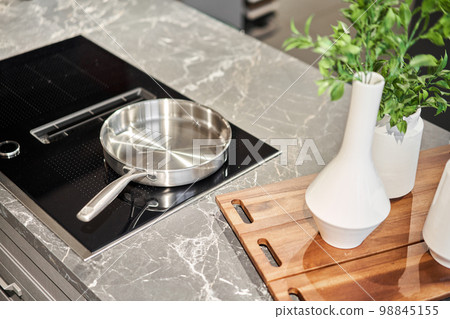 New cookware set on black induction hob in modern kitchen. Pot and frying pan in the kitchen on the hob. cooking concept - close up of kitchen table with modern equipment New cookware set on black induction hob in modern kitchen. Pot and frying pan in the kitchen on the hob. cooking concept - close up of kitchen table with modern equipment 98845155