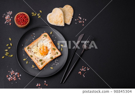 Heart shaped fried egg in bread toast with sesame seeds, flax seeds and pumpkin seeds on a black plate Heart shaped fried egg in bread toast with sesame seeds, flax seeds and pumpkin seeds on a black plate 98845304