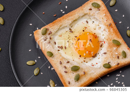 Heart shaped fried egg in bread toast with sesame seeds, flax seeds and pumpkin seeds on a black plate Heart shaped fried egg in bread toast with sesame seeds, flax seeds and pumpkin seeds on a black plate 98845305