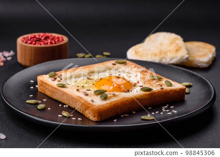 Heart shaped fried egg in bread toast with sesame seeds, flax seeds and pumpkin seeds on a black plate Heart shaped fried egg in bread toast with sesame seeds, flax seeds and pumpkin seeds on a black plate 98845306