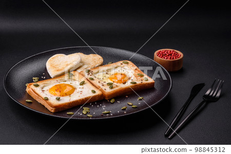 Heart shaped fried egg in bread toast with sesame seeds, flax seeds and pumpkin seeds on a black plate Heart shaped fried egg in bread toast with sesame seeds, flax seeds and pumpkin seeds on a black plate 98845312