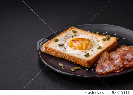 Heart shaped fried egg in bread toast with sesame seeds, flax seeds and pumpkin seeds on a black plate Heart shaped fried egg in bread toast with sesame seeds, flax seeds and pumpkin seeds on a black plate 98845318