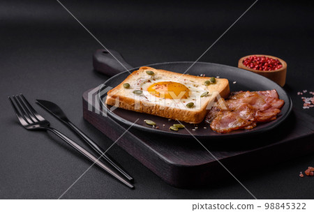 Heart shaped fried egg in bread toast with sesame seeds, flax seeds and pumpkin seeds on a black plate Heart shaped fried egg in bread toast with sesame seeds, flax seeds and pumpkin seeds on a black plate 98845322