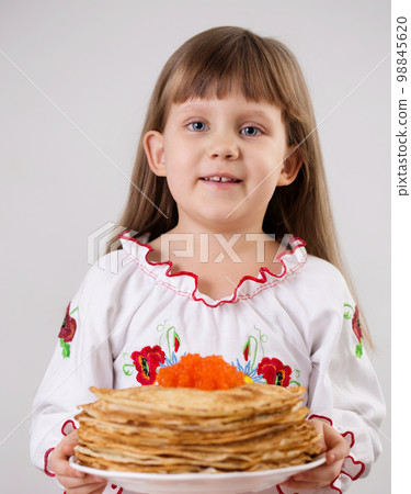 A girl in a Ukrainian embroidered dress is holding pancakes with red caviar A girl in a Ukrainian embroidered dress is holding pancakes with red caviar 98845620