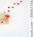 Valentine's Day flatlay. Gift box of craft paper with hearts and red flowers on the white wooden background. 98847308