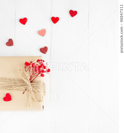 Valentine's Day flatlay. Gift box of craft paper with hearts and red flowers on the white wooden background. 98847311